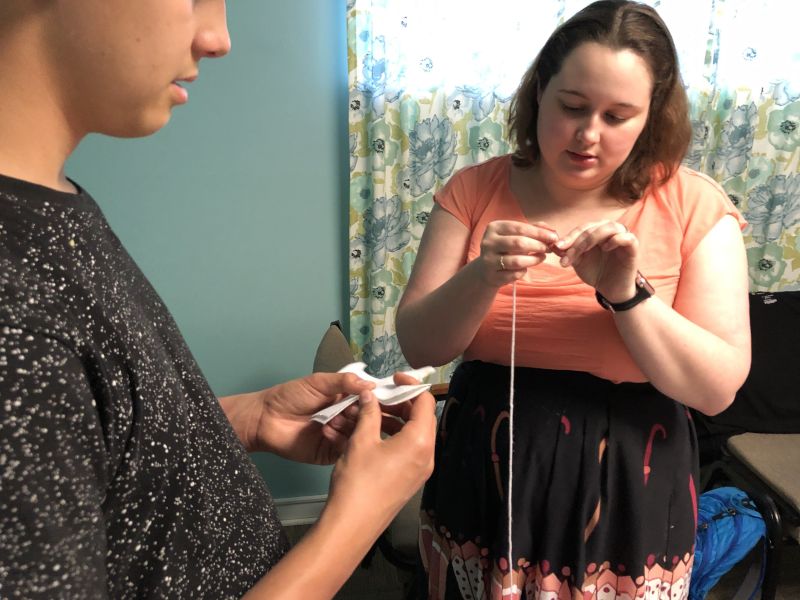 Ariel Teaching a Young Man How to Sew